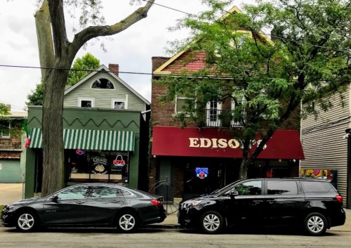 A street view featuring two parked cars in front of a building with a red awning labeled "EDISON'S" and a green-striped storefront.