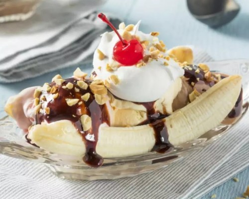 A banana split topped with ice cream, chocolate sauce, whipped cream, chopped nuts, and a cherry.