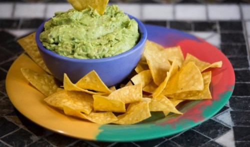 A bowl of guacamole surrounded by tortilla chips on a colorful plate.