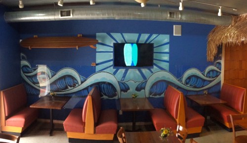 A colorful restaurant interior featuring wave murals, red booths, and a TV on a blue wall.