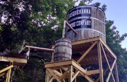 A wooden water tower with a sign reading "Susquehanna Mining Company," supported by a wooden structure and barrels.