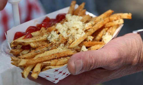 A hand holding a tray of golden fries topped with herbs and cheese, accompanied by a side of ketchup.