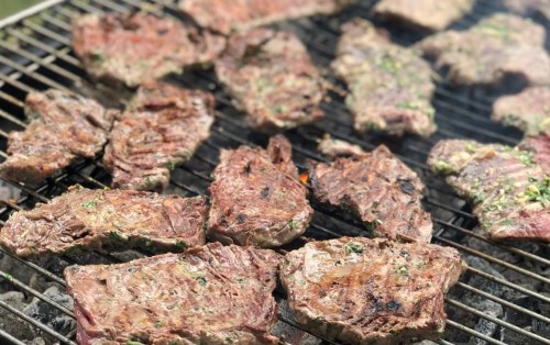 Grilled steaks sizzling on a barbecue grill, showcasing a variety of cooked meat with a smoky flavor.
