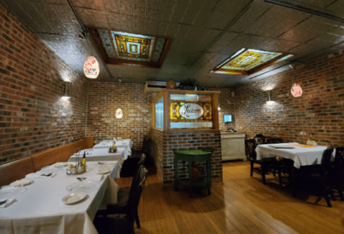 Cozy restaurant interior with brick walls, stained glass, and white tablecloths on wooden tables.