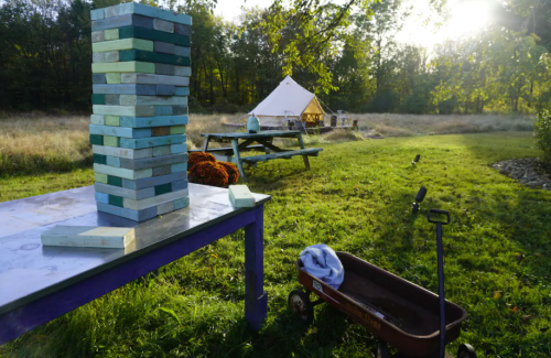 A colorful Jenga tower on a table in a grassy field, with a tent and picnic area in the background.