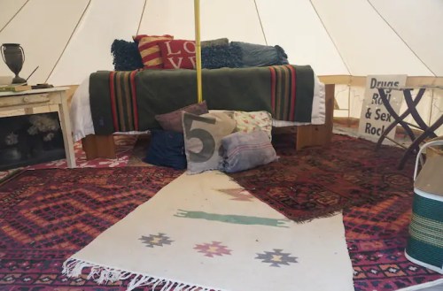 Cozy interior of a tent featuring a bed, colorful pillows, rugs, and a decorative sign.