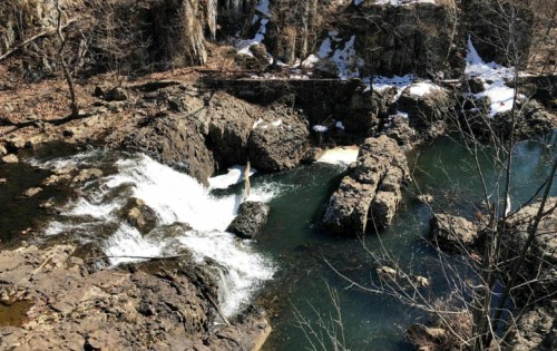 A scenic view of a waterfall cascading over rocky terrain, surrounded by bare trees and a calm river.