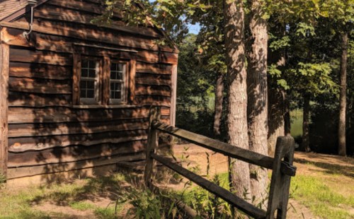 A rustic wooden cabin surrounded by trees and a wooden fence in a serene outdoor setting.