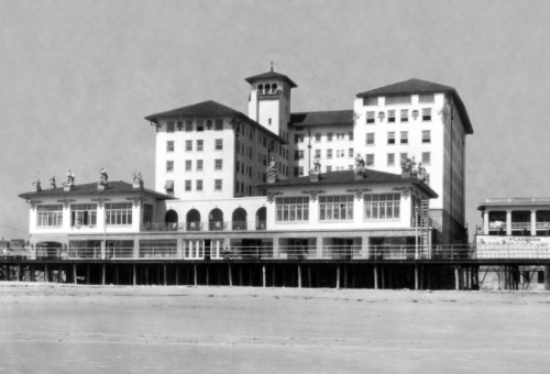 Historic black-and-white photo of a large seaside hotel with multiple stories and a wooden pier.