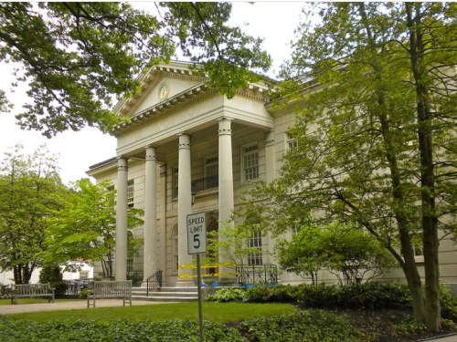 Historic building with columns, surrounded by trees and benches, featuring a speed limit sign in the foreground.