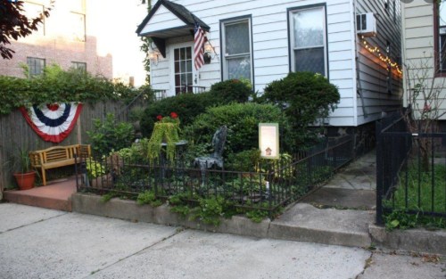A quaint house with a garden, featuring a bench, greenery, and patriotic decorations on the fence.
