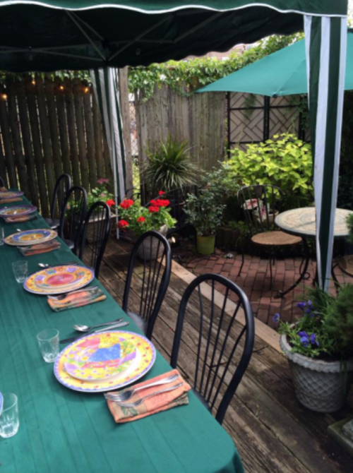 A cozy outdoor dining setup with a long table, colorful plates, and lush greenery in a garden setting.