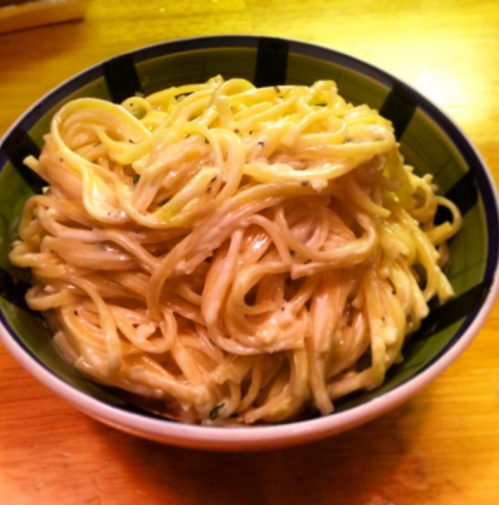 A bowl of creamy spaghetti, lightly coated in a rich sauce, served on a wooden table.
