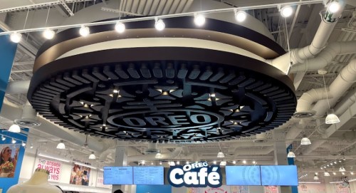 A large Oreo cookie sign hangs from the ceiling above the Oreo Café, featuring the brand's logo and decorative design.