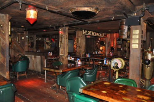 Interior of a rustic bar named "Sea Venture," featuring wooden decor, green chairs, and nautical-themed elements.
