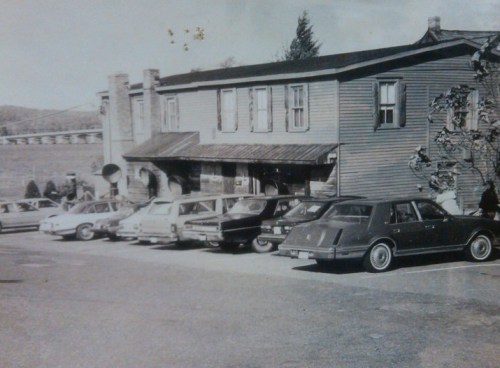 Black and white photo of a vintage building with several classic cars parked in front.