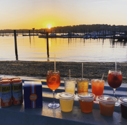 A sunset over a marina with various colorful drinks lined up on a ledge.