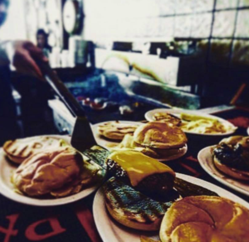 A close-up of a grill with burgers and cheese on plates, ready to be served in a bustling kitchen.