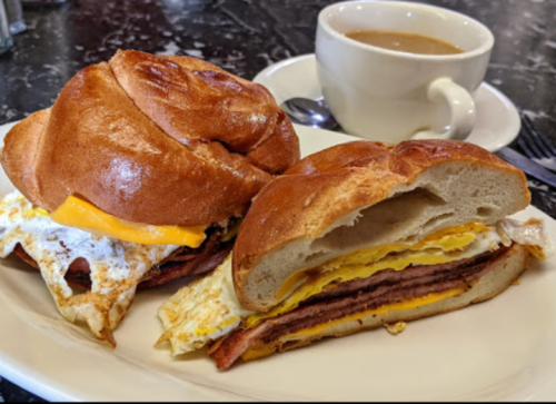 A plate with two breakfast sandwiches featuring eggs, cheese, and meat, alongside a cup of coffee.