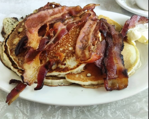 A plate of pancakes topped with crispy bacon, served with a dollop of butter on the side.