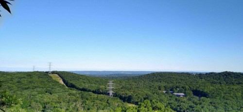 A panoramic view of lush green hills under a clear blue sky, with power lines stretching across the landscape.