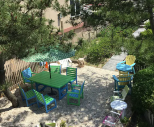 A colorful outdoor seating area with a green table and chairs, surrounded by trees and a gravel path.