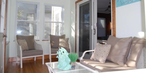 Bright sunroom with two chairs, a table, and decorative accents, featuring large windows and light wooden flooring.