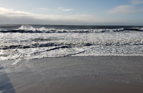 Waves crashing on a sandy beach under a clear sky, with a gentle shoreline and distant horizon.