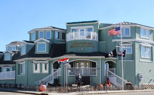 A coastal building with a blue exterior, featuring flags and a sign for a maritime museum.
