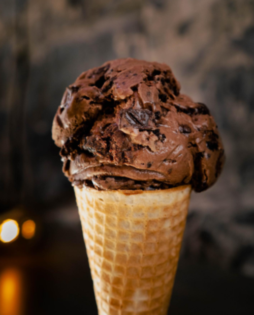 A close-up of a chocolate ice cream scoop on a waffle cone against a blurred background.