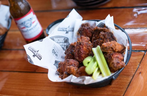 A basket of crispy fried chicken wings with celery sticks, next to a bottle of beer on a wooden table.