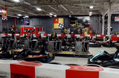 Indoor go-kart track with multiple karts lined up, red and white barriers, and a checkered flag backdrop.