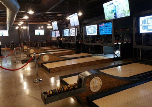 Interior of a bowling alley with multiple lanes, screens, and seating areas, featuring a modern design.