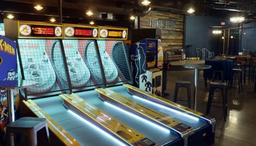 A vibrant arcade with a skee-ball machine and a retro game cabinet in a lively social space.