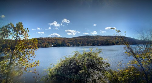 A serene lake surrounded by autumn foliage under a clear blue sky with fluffy white clouds.
