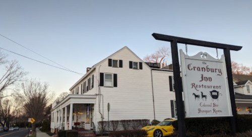 A white building with a sign reading "The Cranbury Inn Restaurant" and a yellow car parked nearby.
