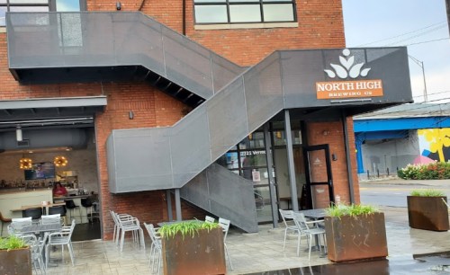 Exterior of North High Brewing Co. featuring a metal staircase, outdoor seating, and a brick building.