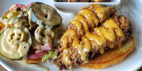 A plate featuring a crispy fried chicken sandwich topped with cheese, alongside a side of pickled vegetables.