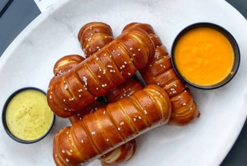 A plate of golden-brown pretzel bites with two dipping sauces: yellow cheese and mustard.