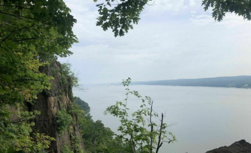 A scenic view of a river surrounded by lush greenery and rocky cliffs under a cloudy sky.