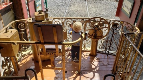 A young child stands at the controls of a vintage train engine, looking out over the tracks.