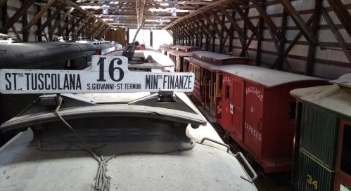 A view inside a train shed filled with vintage train cars and a sign reading "16 St. T. Tuscolana."