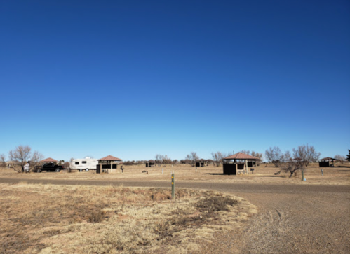 A wide view of a rural area with several small buildings and an RV under a clear blue sky.