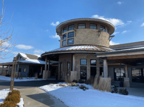 A modern stone building with a circular design, surrounded by snow and blue skies.