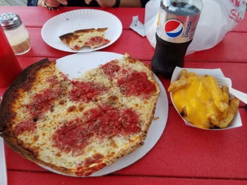 A large slice of pizza with sauce and cheese, a side of cheese fries, and a bottle of Pepsi on a red table.
