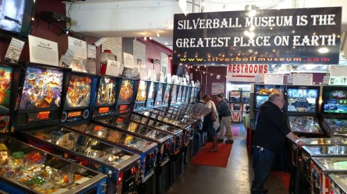 A vibrant arcade with rows of pinball machines and a sign reading "Silverball Museum is the Greatest Place on Earth."