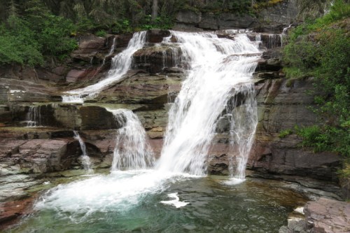 A serene waterfall cascading over rocky cliffs into a clear pool, surrounded by lush greenery.