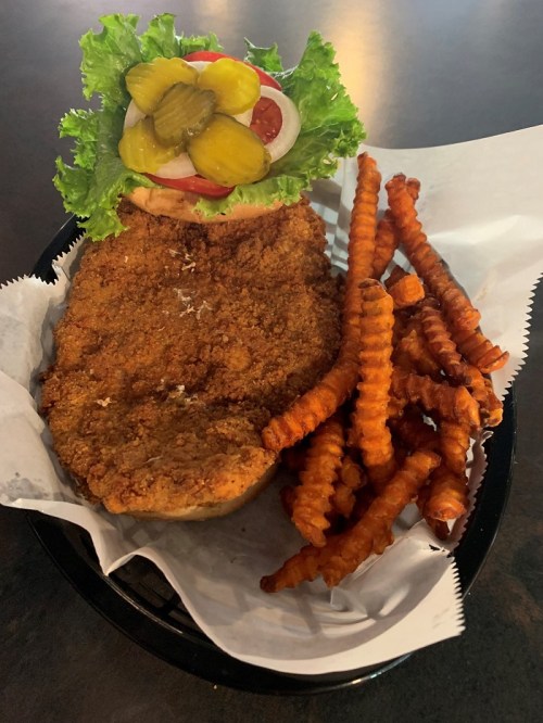 A crispy fried chicken sandwich topped with lettuce, tomato, and pickles, served with sweet potato fries.