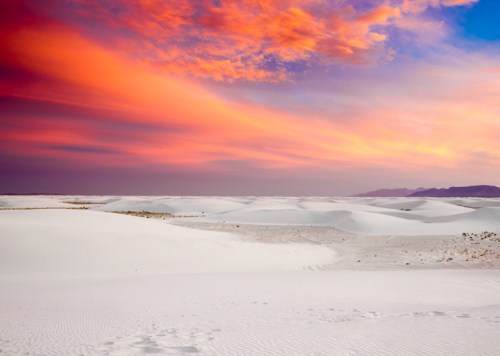 A vast white desert under a vibrant sunset sky with shades of orange, pink, and purple.