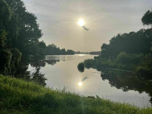 A serene river scene at sunset, with reflections on the water and lush greenery along the banks.